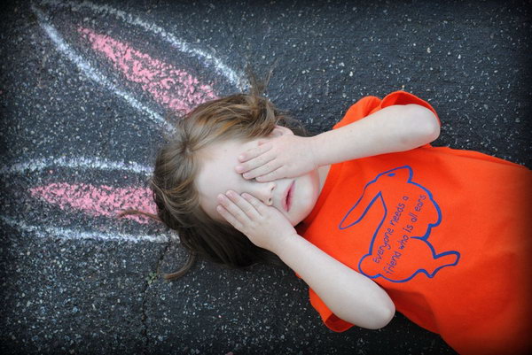 Funny Bunny Ears Easter Photo. The little girl wearing a red T-shirt with a bunny patter is lying on the ground with the bunny ears drawing beforehand. I really love this Easter photo idea, it’s full of creation and imagination.